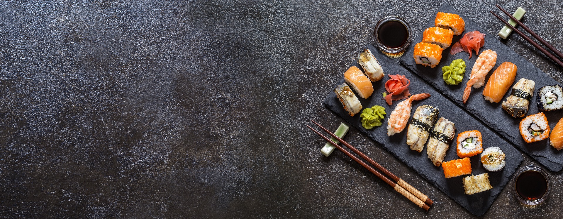 sushi rolls with rice and fish, soy sauce on a dark stone background